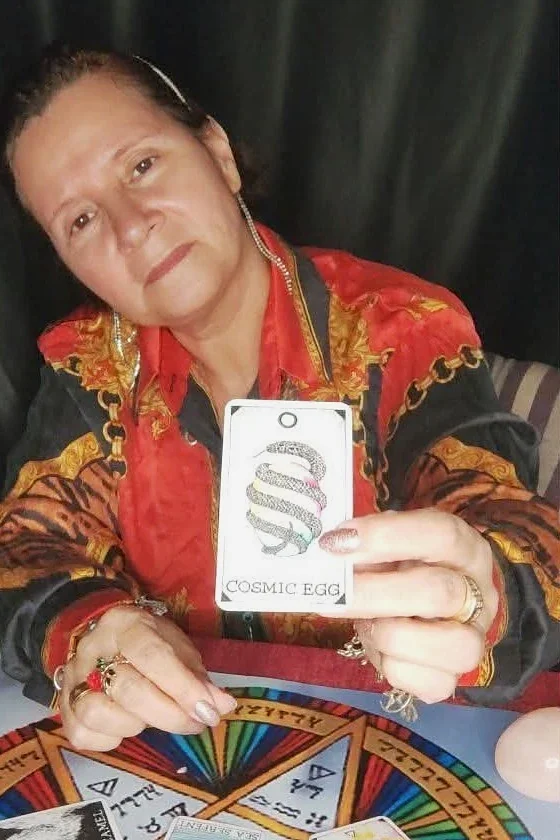 A Liz à mesa de atendimento, mostrando a carta Cosmic Egg sobre a mandala colorida